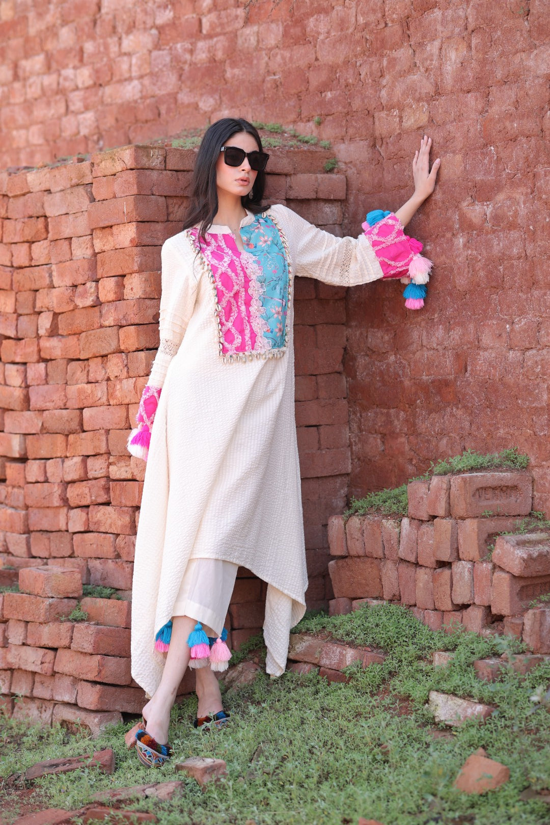 Model wearing ivory asymmetrical kurta with multicolour embroidered yoke and tassel pants