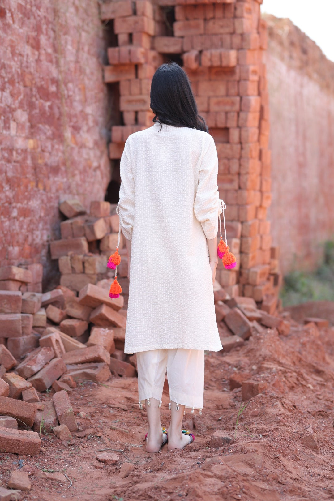 Clean ivory kurta back with subtle texture, paired with straight pants, against a red brick wall.