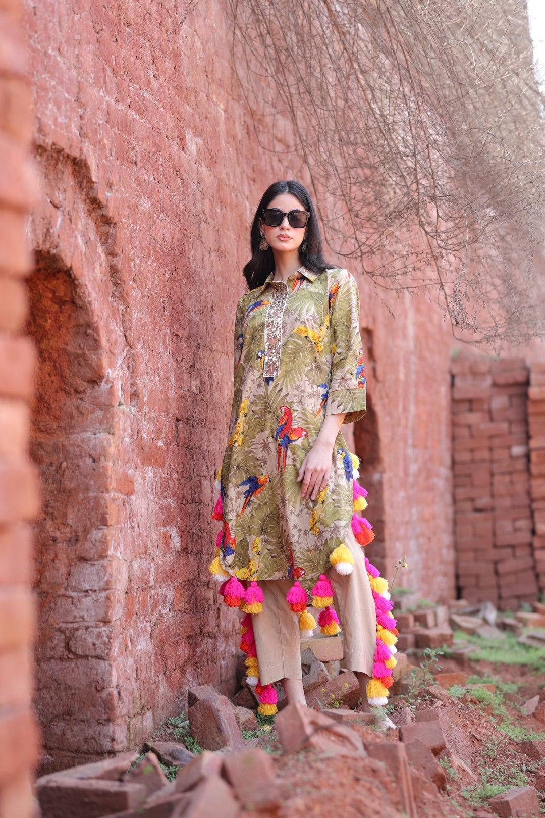 Model in tropical parrot kurta with vibrant tassels standing against brick wall