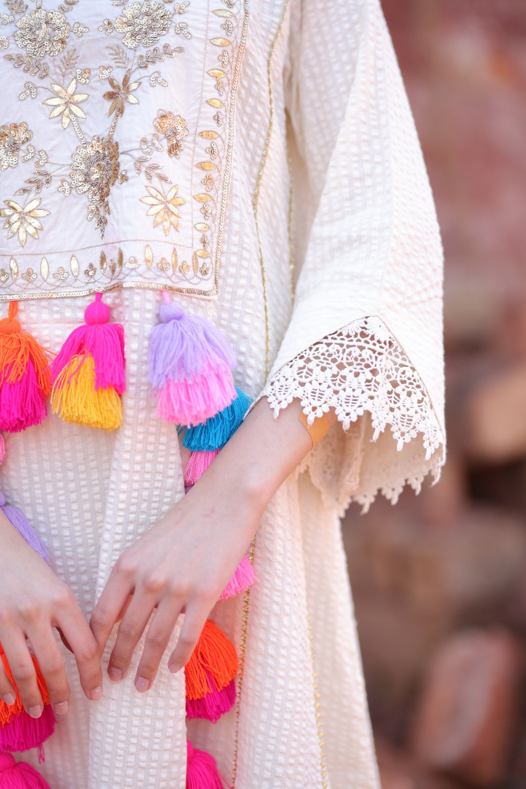 Close-up of gold embroidery and colourful handmade tassels on ivory base