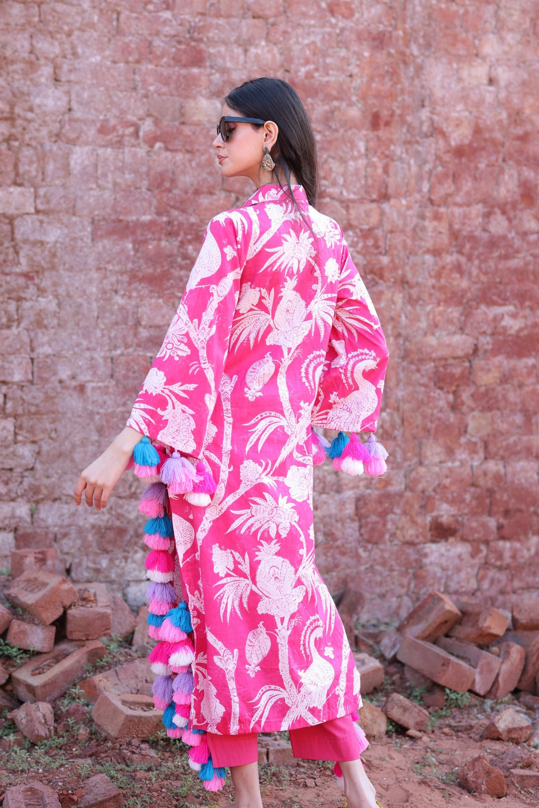 Back view of tasselled pink kurta against earthy brick wall